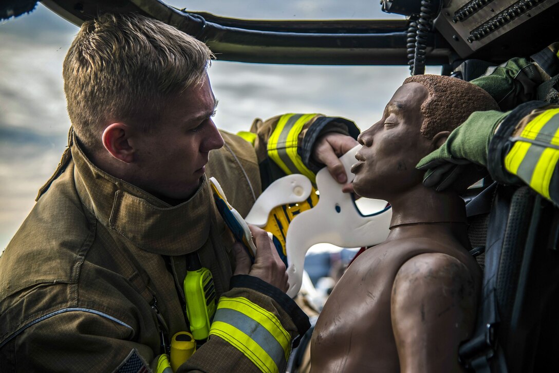 An airman faces a mannequin in a vehicle and puts a neck brace on it.