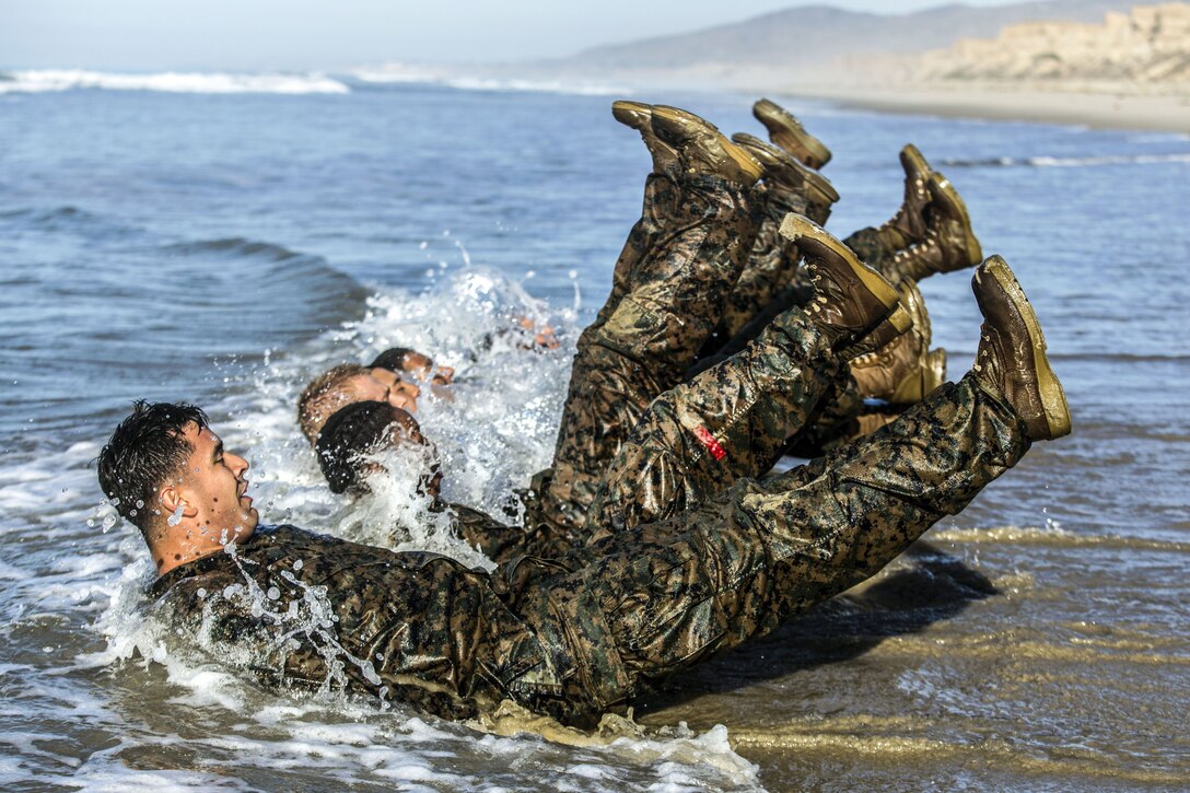 Marines kick while lying face up in a row in ocean water.