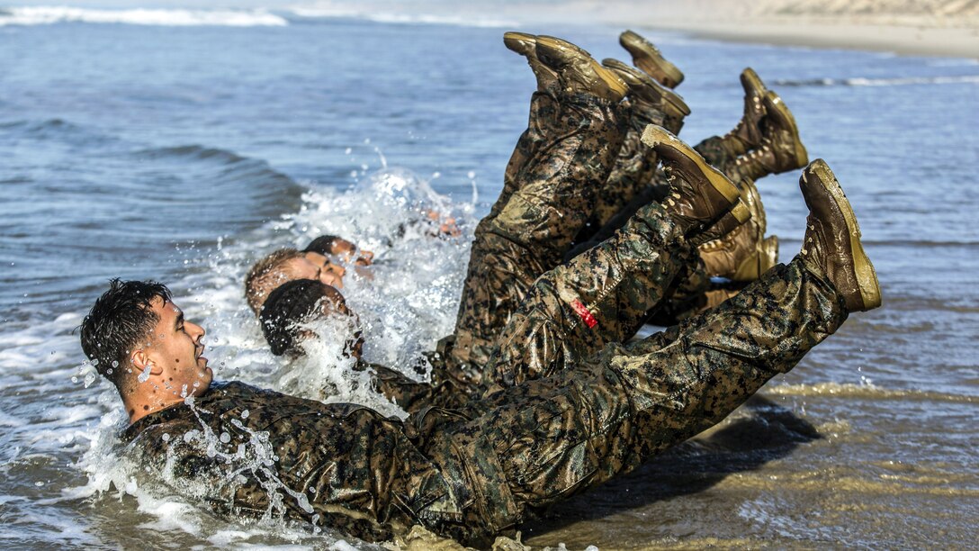 Marines kick while lying face up in a row in ocean water.