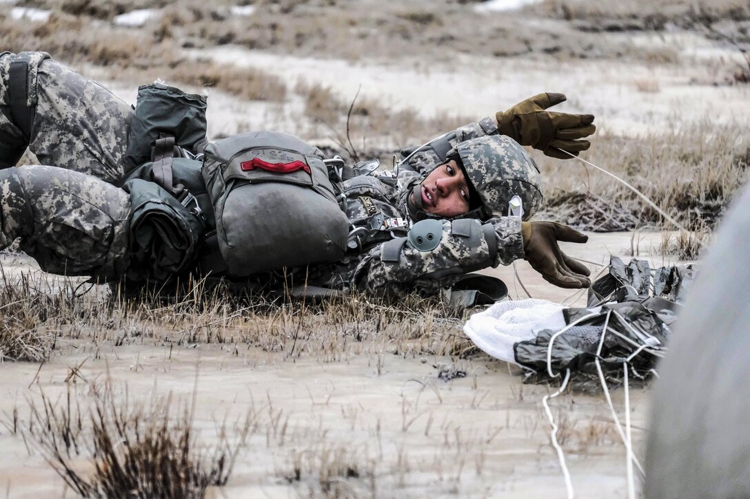 A soldier lies on the ground and reaches his arms above his head.