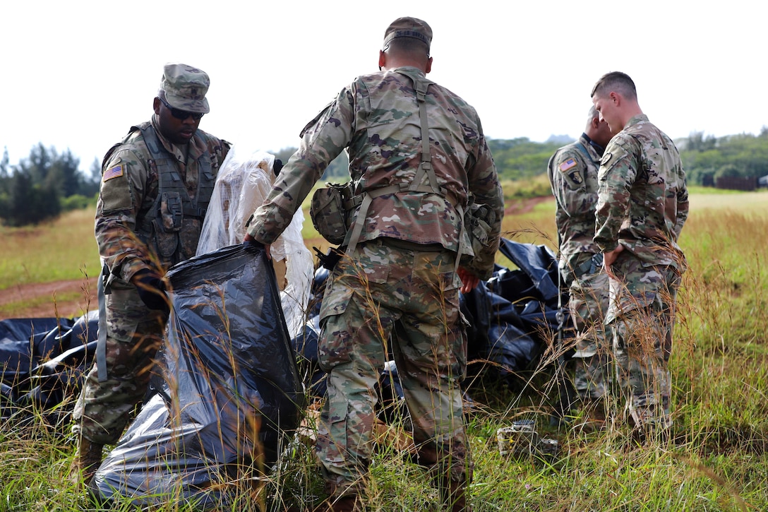 Soldiers pick up cargo matting material left over from the low cost low altitude loads air dropped from a CH-47 Chinook helicopter.