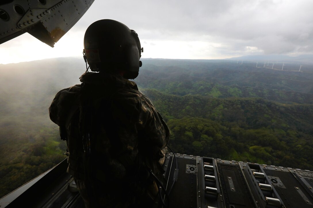 Army Spc. Logan Mattix looks out at the Hawaiian mountain range from the back ramp of a CH-47 Chinook helicopter.