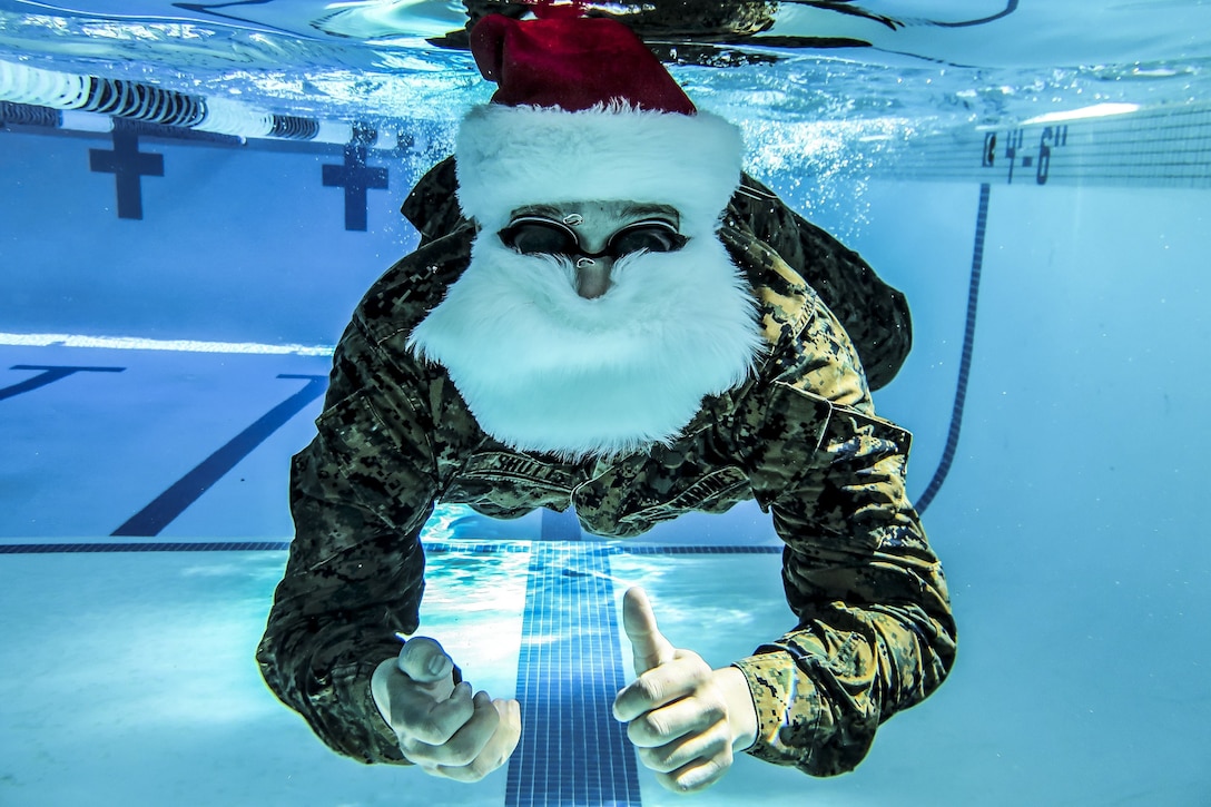 A Marine in a Santa Claus suit swims underwater in a pool.