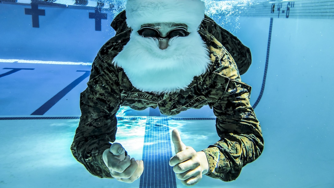 A Marine in a Santa Claus suit swims underwater in a pool.