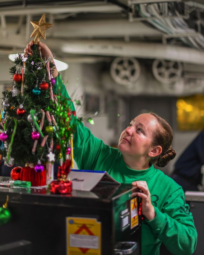 A sailor decorates a Christmas tree.