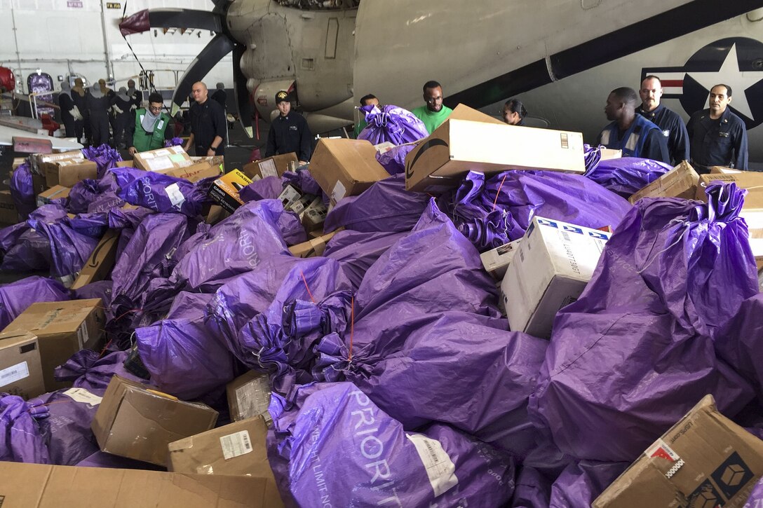 Sailors sort purple bags of incoming mail on a ship.