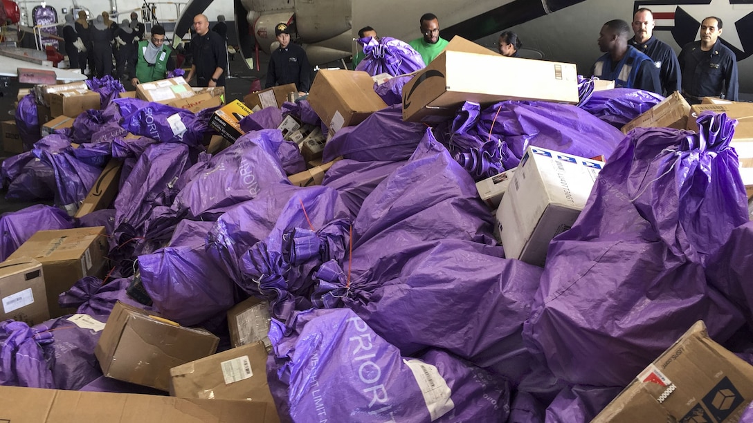 Sailors sort purple bags of incoming mail on a ship.