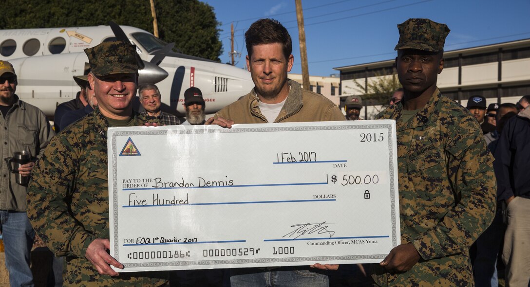 U.S. Marine Corps Col. Ricardo Martinez (left), the commanding officer of Marine Corps Air Station Yuma, Ariz., and Sgt. Maj. Delvin Smythe (right), the sergeant major of MCAS Yuma, award Brandon Dennis (center), a high voltage electrician with Installation & Logistics, a check for five hundred dollars in addition to the MCAS Yuma Employee of the Quarter award in front of the station headquarters, Feb. 1, 2017. (U.S. Marine Corps photo taken by Lance Cpl. Christian Cachola/Released)