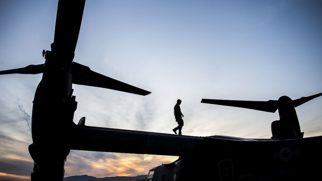 A silhouetted airman walks on a CV-22 Osprey helicopter before a training mission.