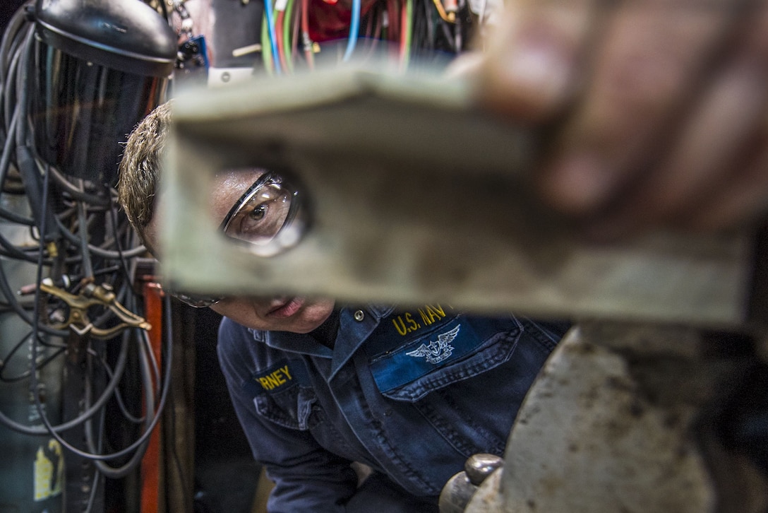 A sailor examines her work after drilling a hole on a ship.