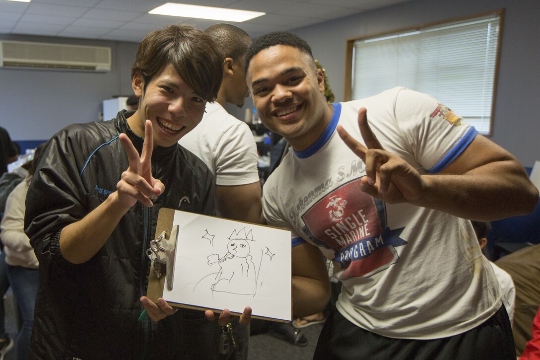 MCAS FUTENMA, OKINAWA, Japan— Nozomu Miyagi, left, and Lance Cpl. Malik Miller pose with their drawing after a game of Pictionary in the Single Marine Program building Dec. 17 on Marine Corps Air Station Futenma, Okinawa, Japan.