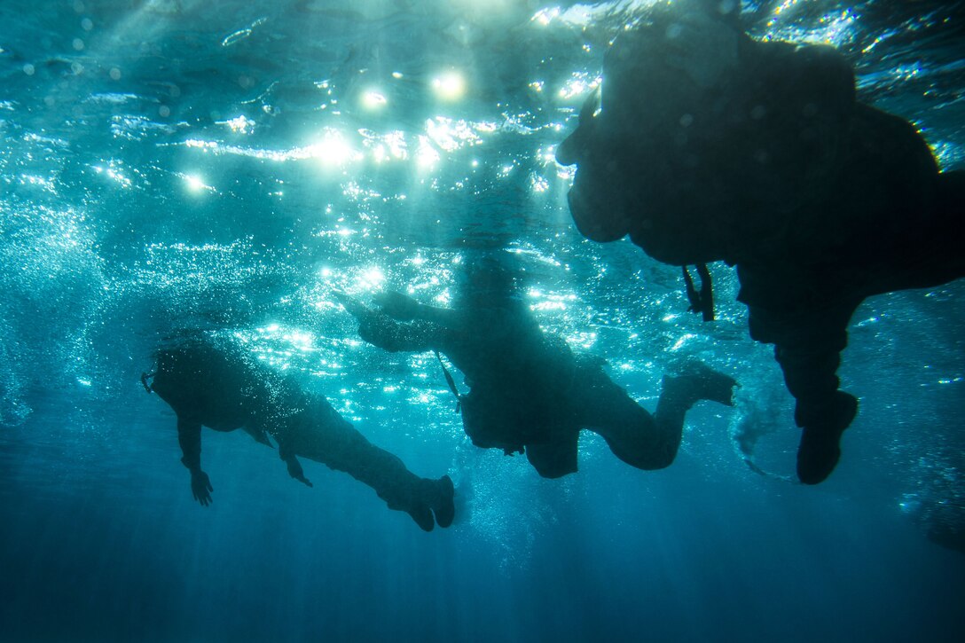 An underwater photo shows Marines sweimming with their gear.