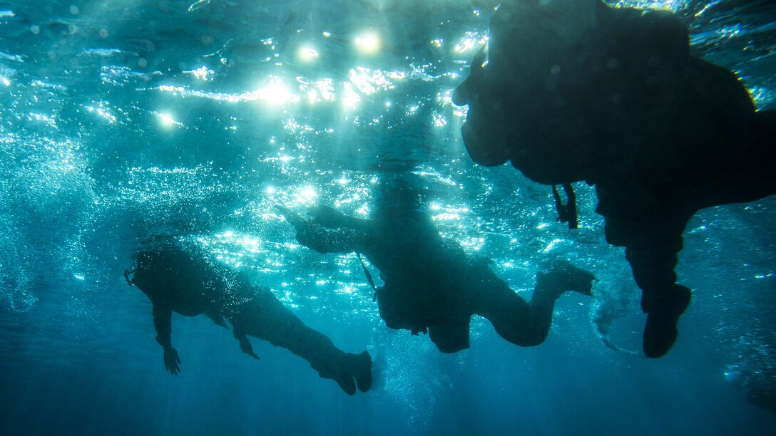 An underwater photo shows Marines sweimming with their gear.