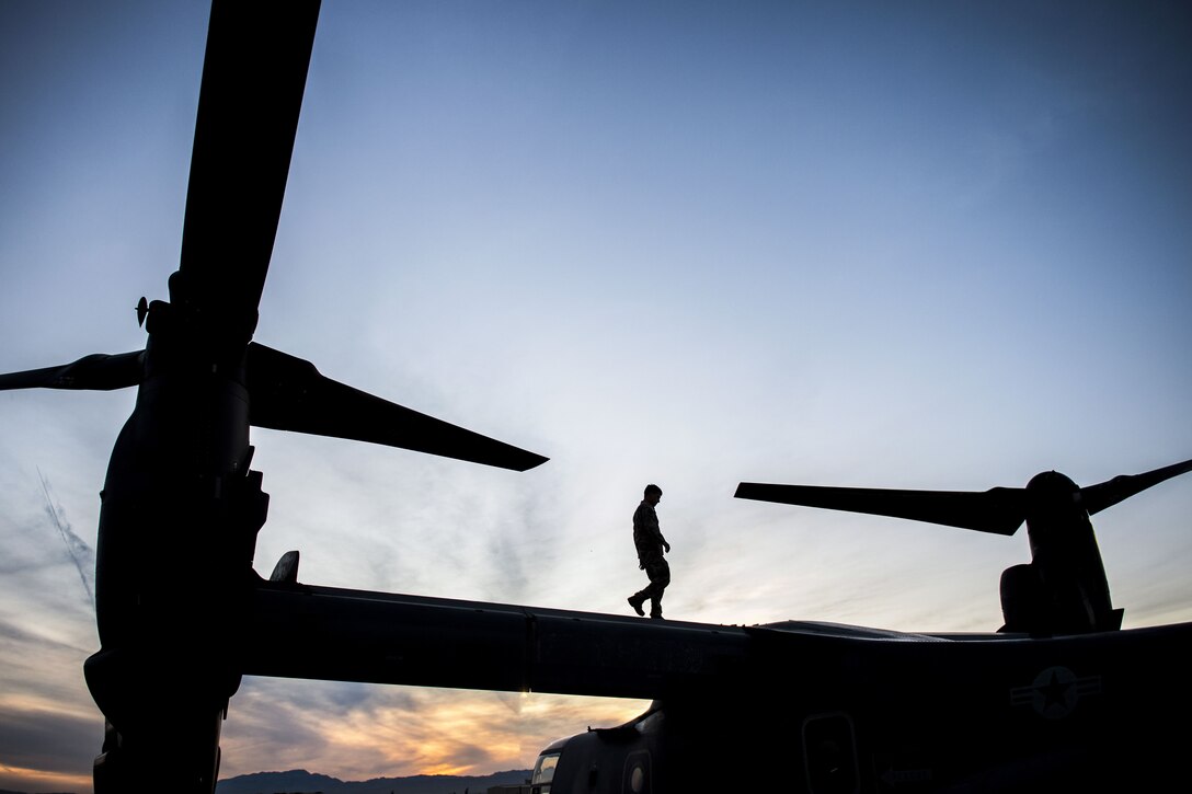 A silhouetted airman walks on a CV-22 Osprey helicopter before a training mission.