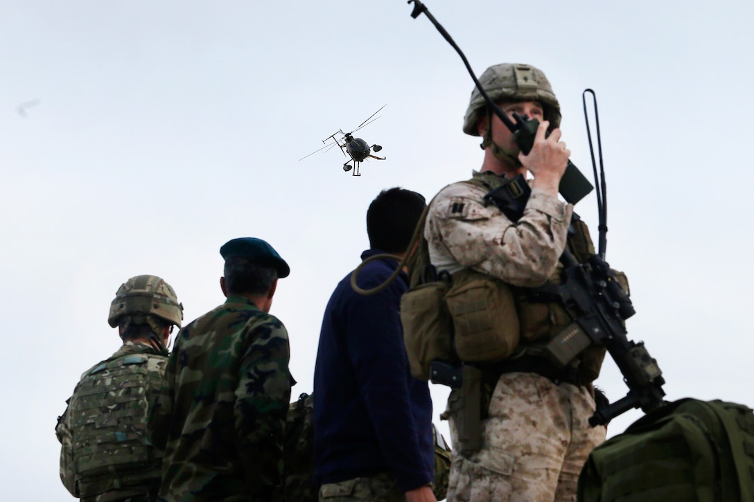 A U.S. Marine talks with his advisory team while a U.S. soldier, left, and Afghan air force tactical air controllers observe an MD-530 helicopter.