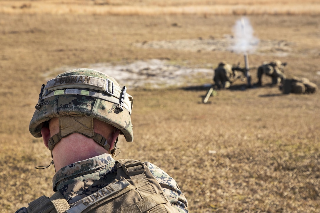 A Marine watches from a distance while two other Marines fire an M224 60 mm mortar system.