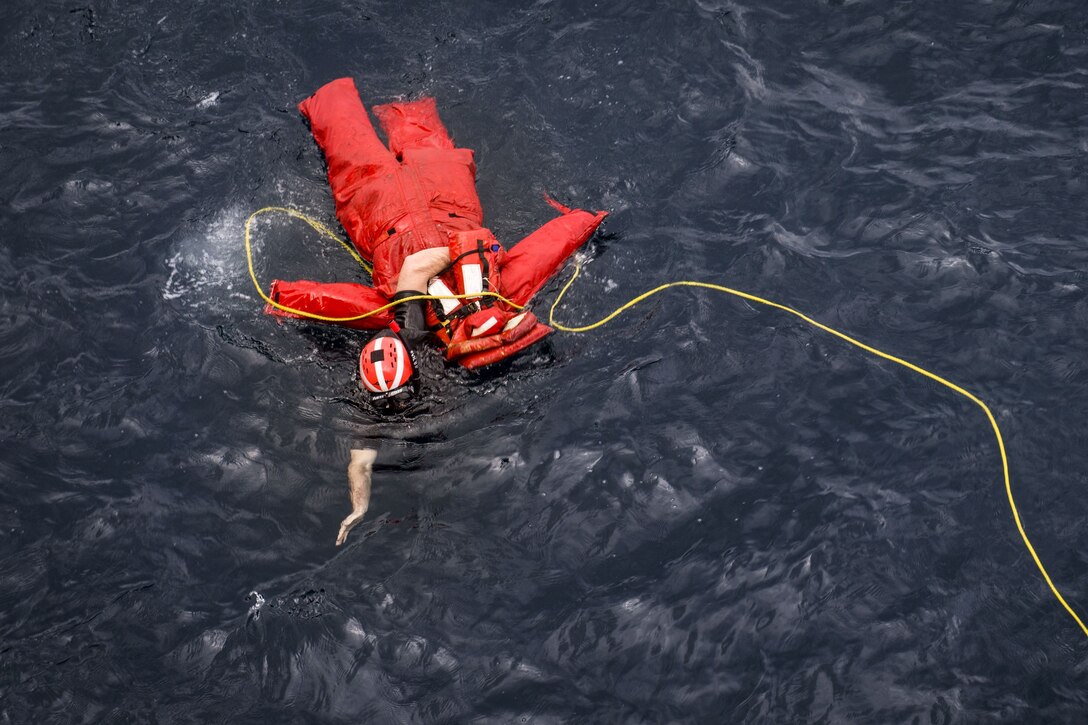 A sailor recovers an orange dummy from the water during a drill.