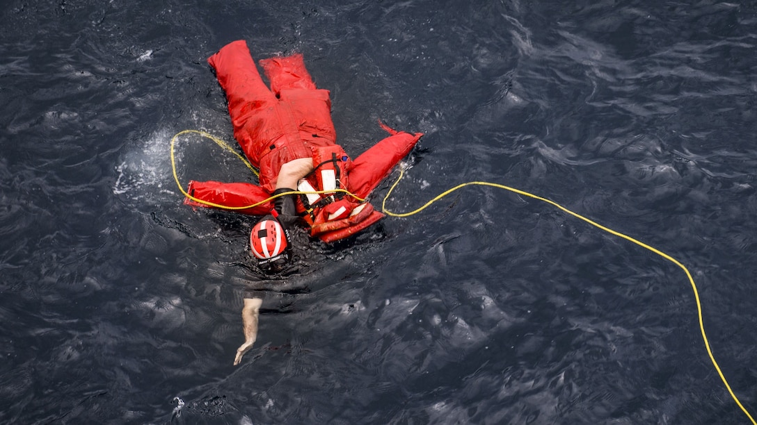 A sailor recovers an orange dummy from the water during a drill.