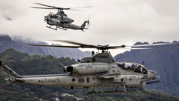 Two helicopters fly over green mountains in Hawaii.