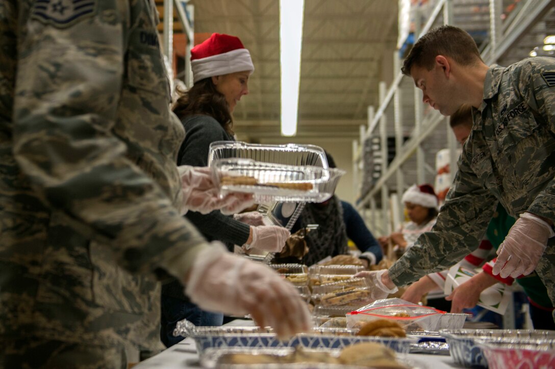 Airmen and volunteers gather cookies on a table.