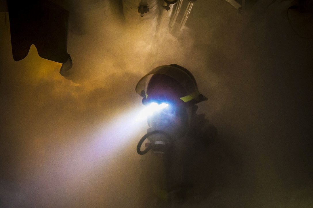 A sailor uses head lights to navigate through a smoky area.