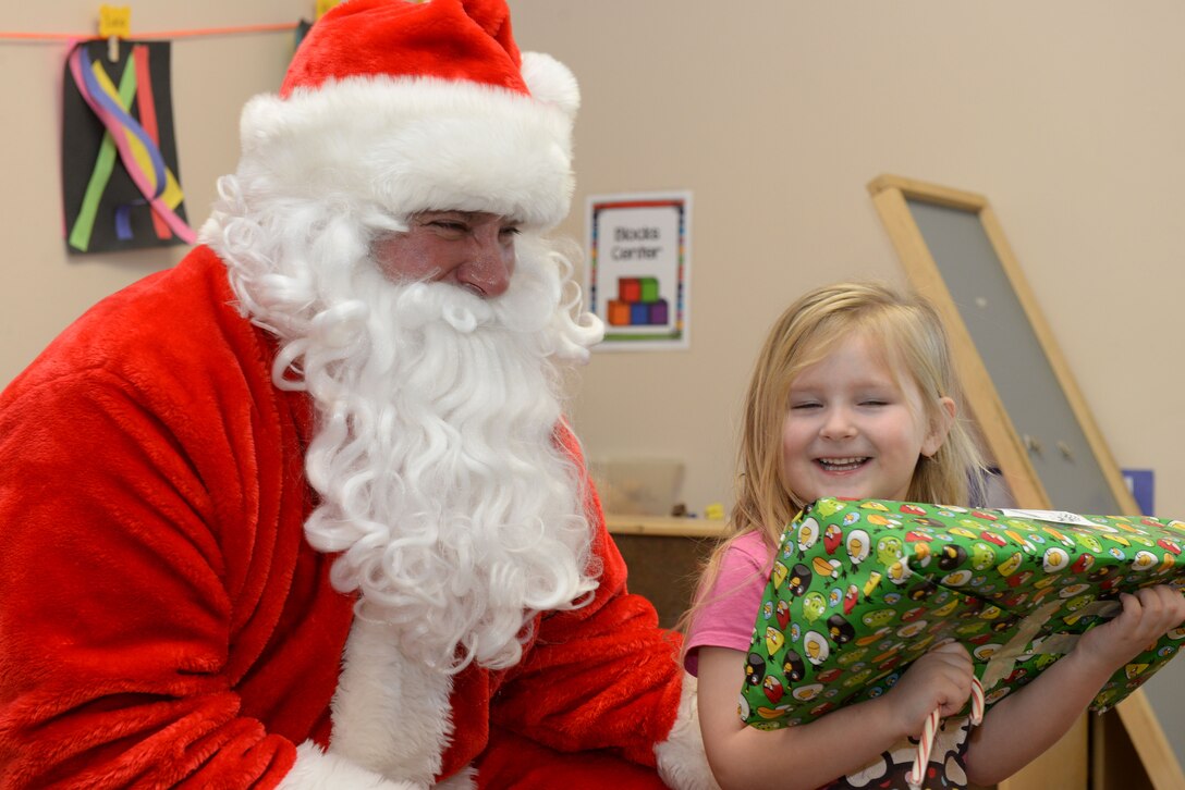 Santa Claus gives a present to a child inside the Youth & Family Services Child Development Center in Rapid City, S.D., Dec. 19, 2017. Ellsworth Airmen have participated in the toy drive for 11 consecutive years. (U.S. Air Force photo by Airman 1st Class Nicolas Z. Erwin)