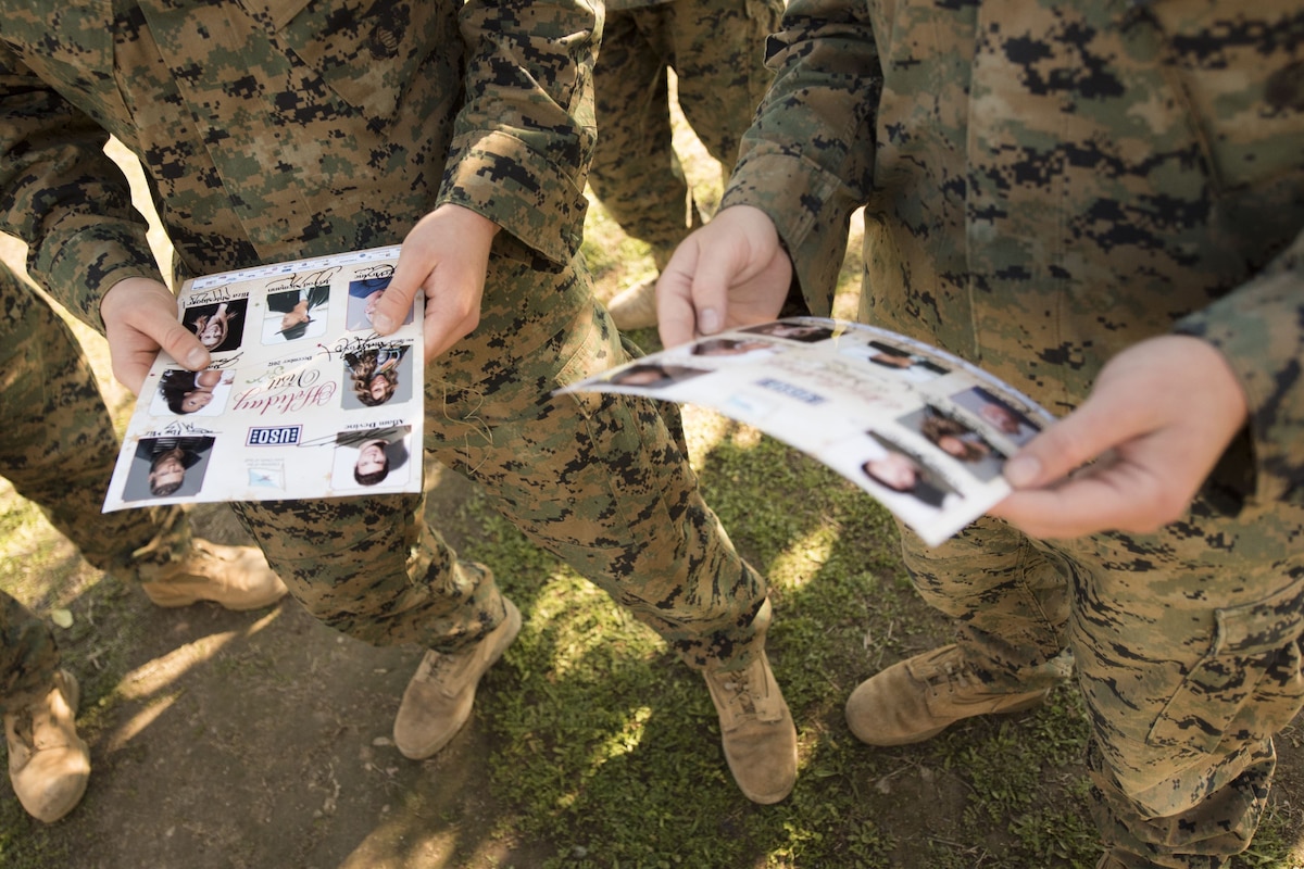 Service members hold a flyer with photos on it.