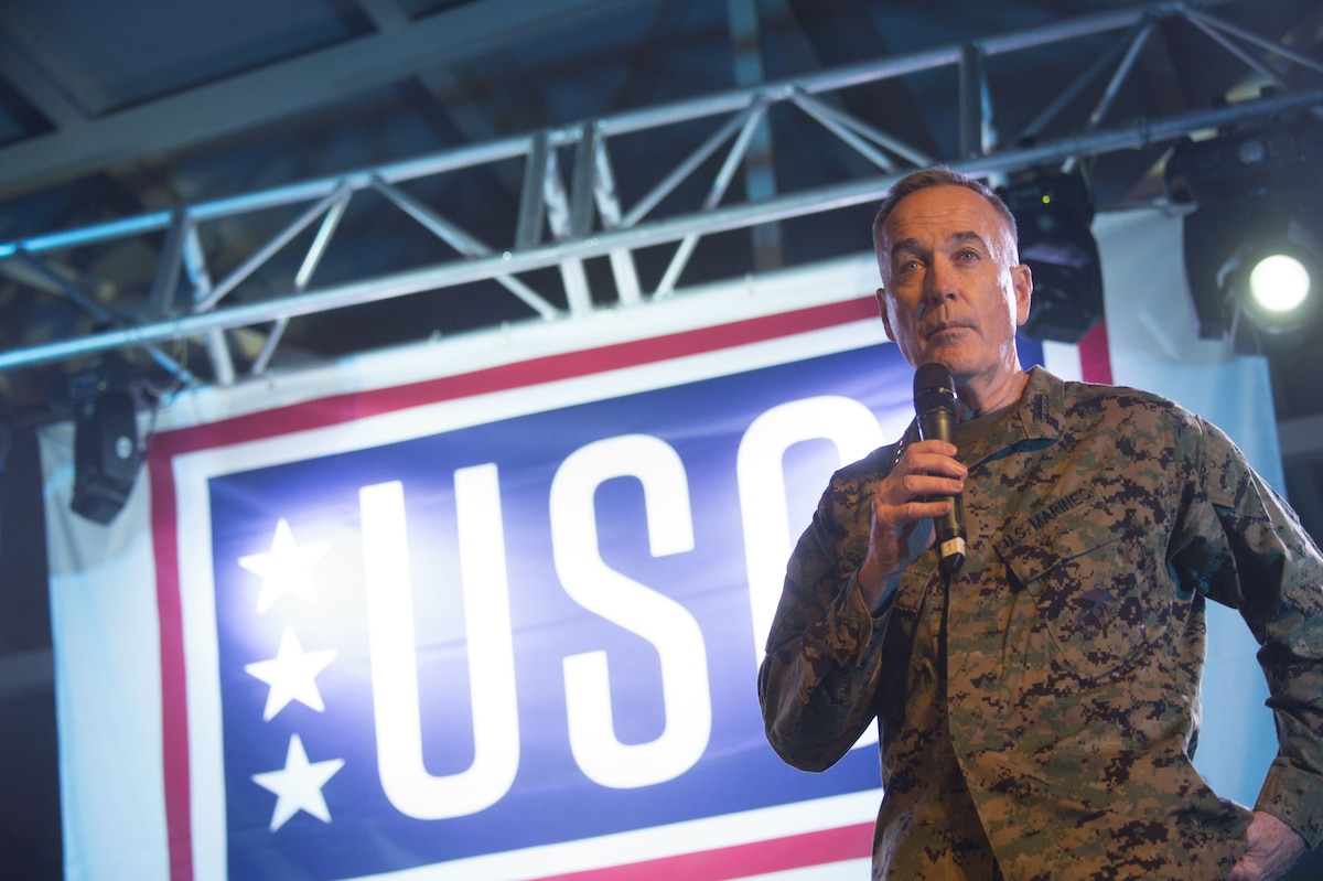 Marine Corps Gen. Joe Dunford speaks on a mic in front of a USO sign.