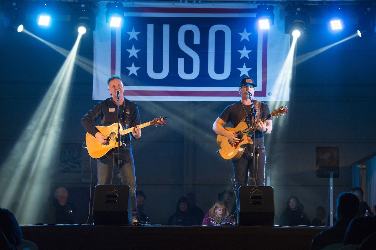 Two men play guitars and sing on stage.