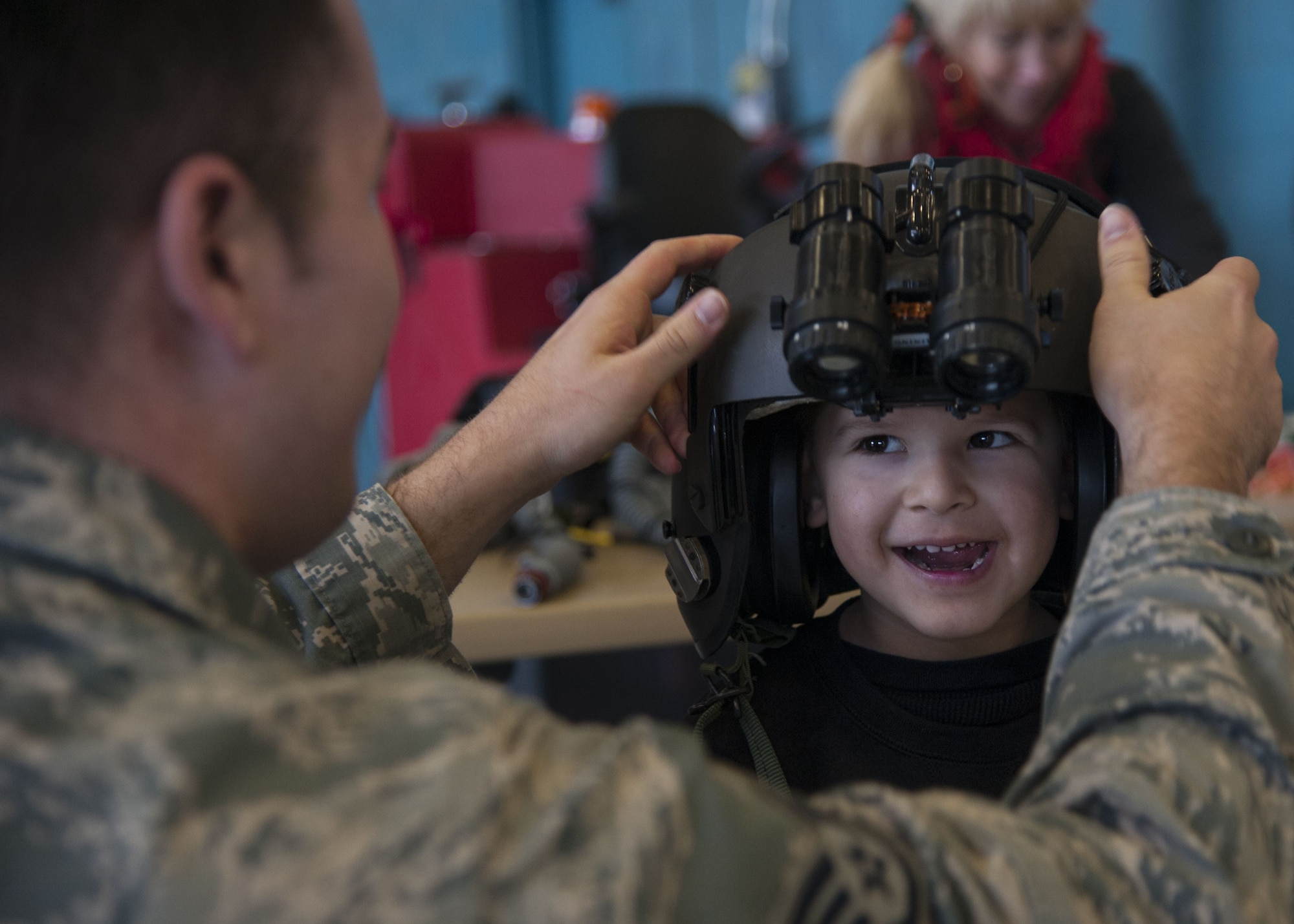 U.S. Air Force Staff Sgt. Mark Guereque, 58th Operations Support Squadron aircrew flight equipment journeymen, adjusts the visor on a helmet for a visitor from the Presbyterian and University of New Mexico children's hospital at Kirtland Air Force Base, N.M., Dec. 21.