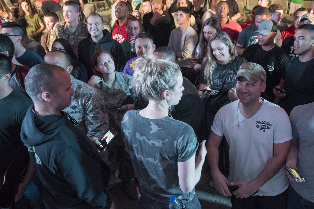 A woman talks to a group of service members standing around her.