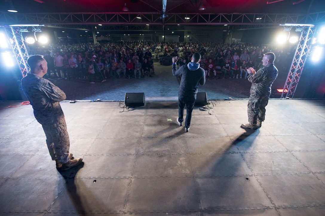 A crowd listens as a speaker delivers remarks on stage, flanked by Marine Corps Gen. Joe Dunford and Army Command Sgt. Maj. John W. Troxell,