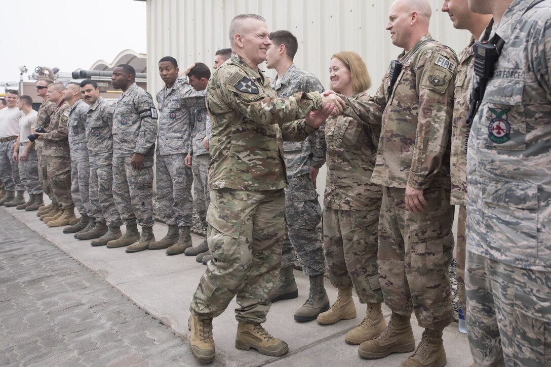 Army Command Sgt. Maj. John W. Troxell shakes hands with a service member standing outside in a row of troops.