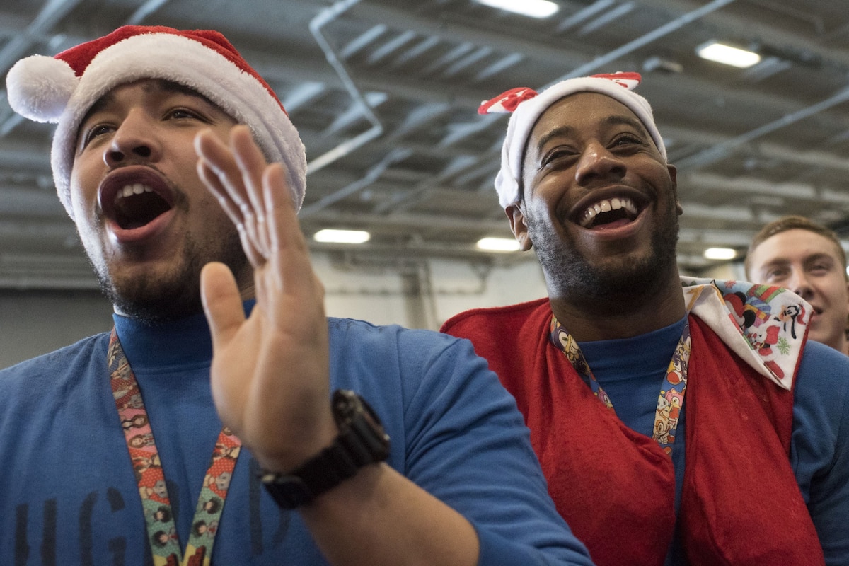 Sailors wearing Santa Claus hats laugh and applaud.
