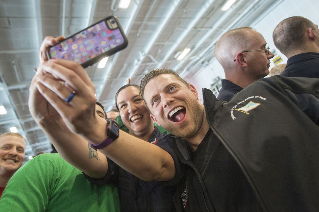 A woman smiles and holds a cell phone in front of her while taking a selifie with WWE Superstar “The Miz."