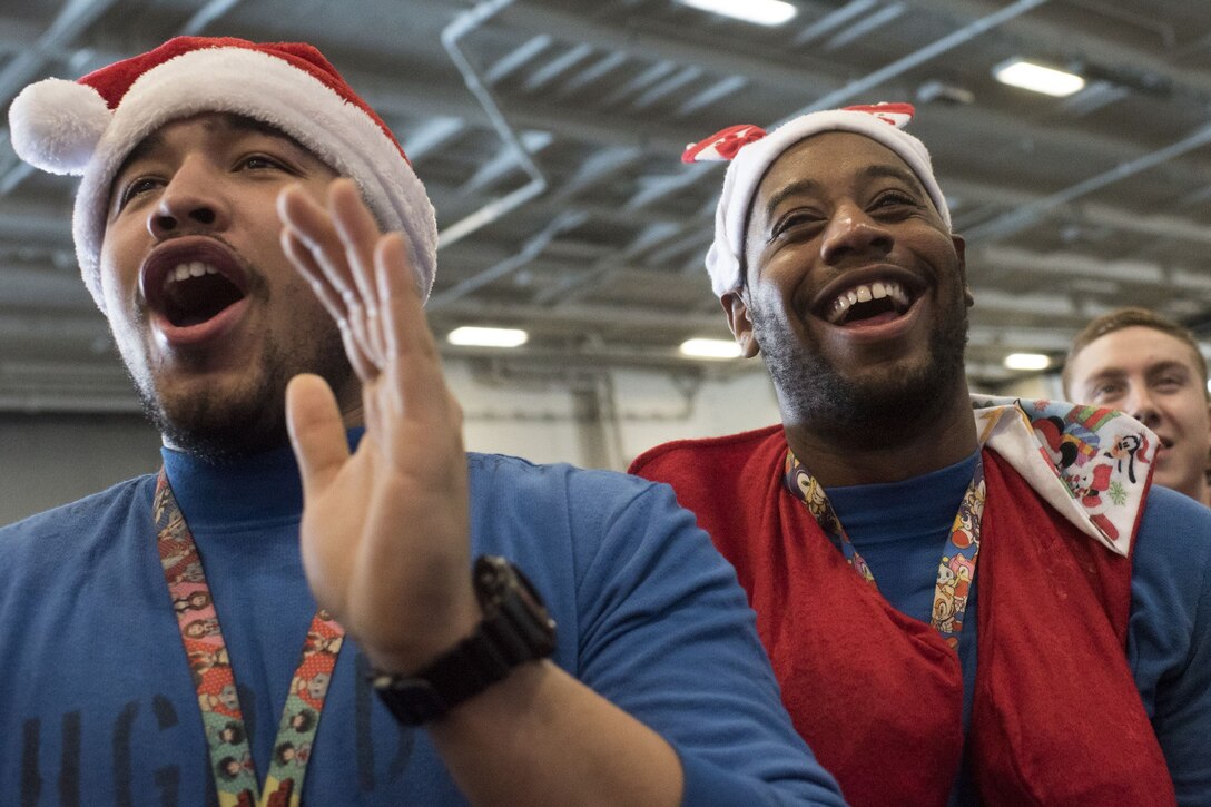 Sailors wearing Santa Claus hats laugh and applaud.