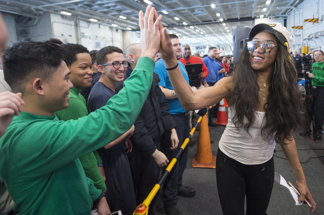 A woman high-fives a sailor while walking past a crowd of troops aboard a ship.