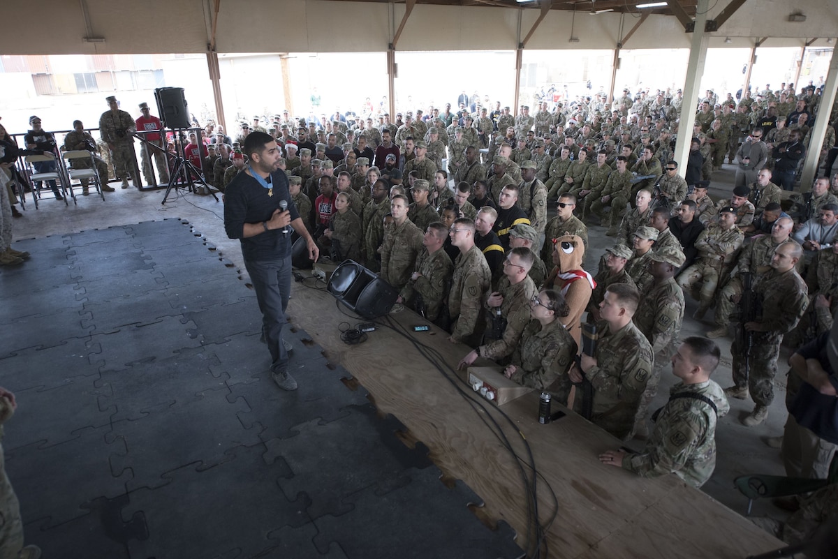 A Medal of Honor recipient stands on stage speaking to service members.