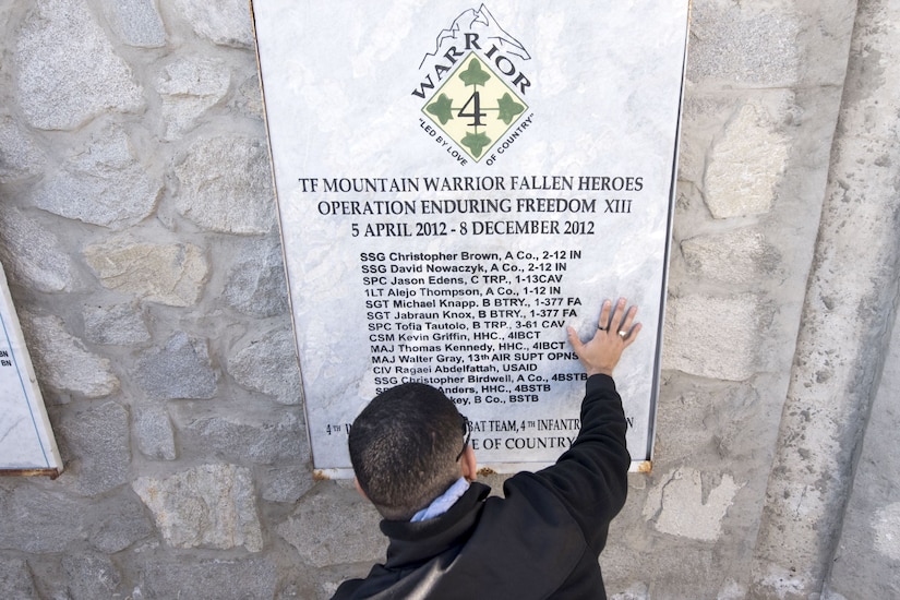 A Medal of Honor recipient kneels at a memorial.