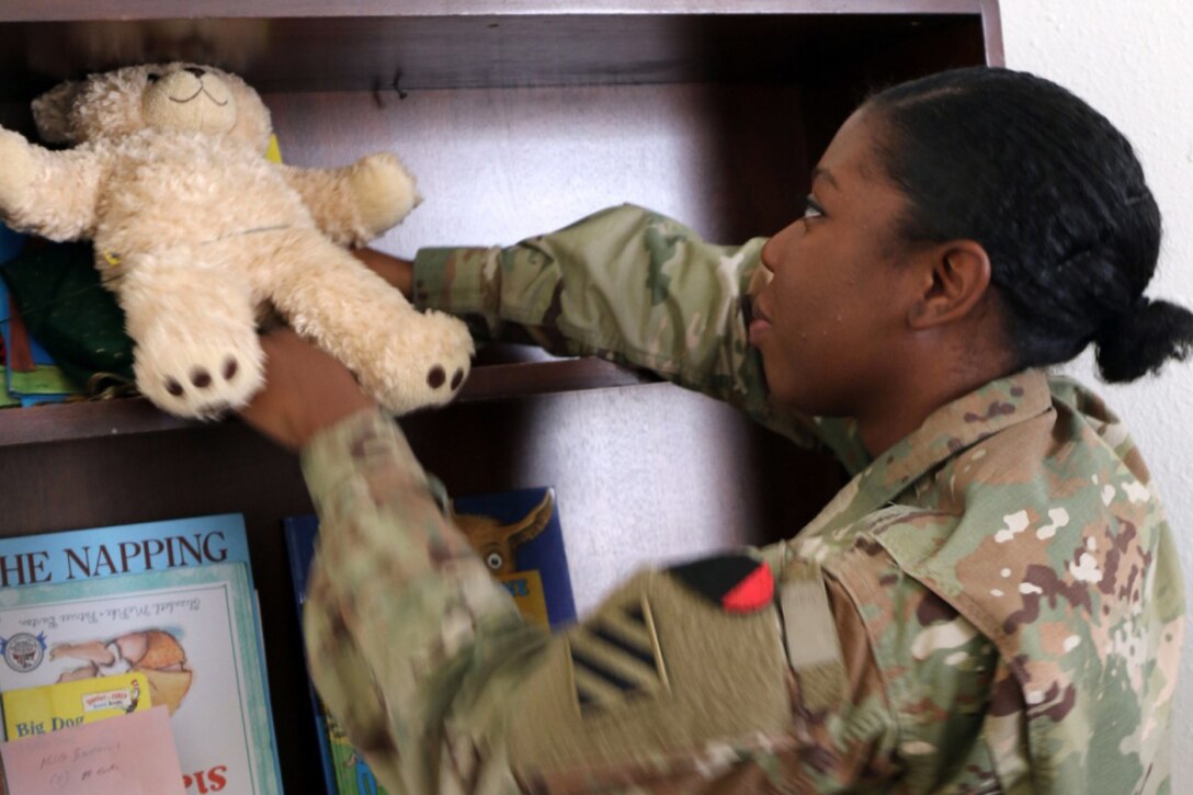 A soldier puts a stuffed bear on a book shelf.