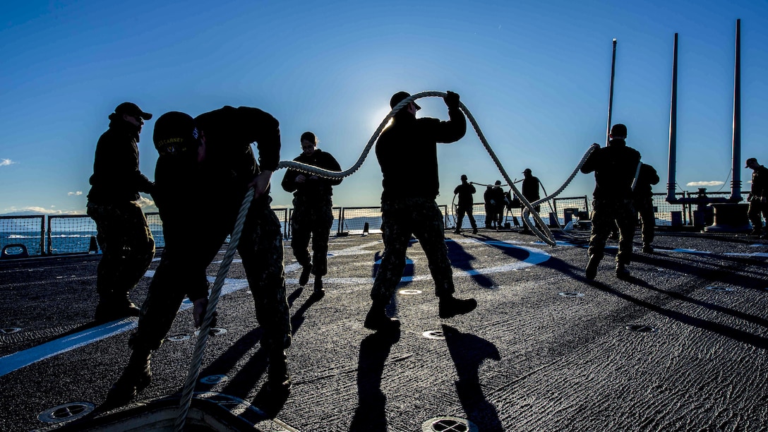 Sailor work on the deck of a ship while silhouetted by the sun.