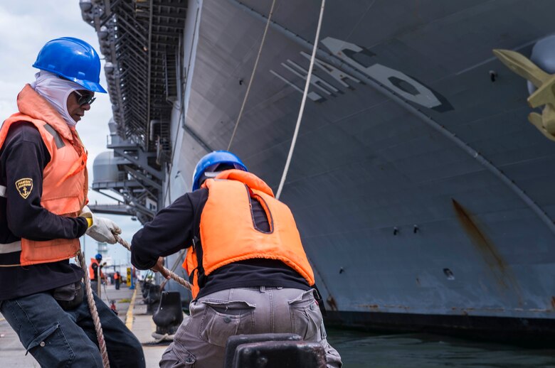 Singaporean contractors moor the amphibious assault ship USS America (LHA 6) as she pulls in to RSS Singapura - Changi Naval Base, Singapore during a regularly scheduled port visit Dec. 22. America, part of the America Amphibious Ready Group, with embarked 15th Marine Expeditionary Unit, is operating in the Indo-Asia Pacific region to strengthen partnerships and serve as a ready-response force for any type of contingency.