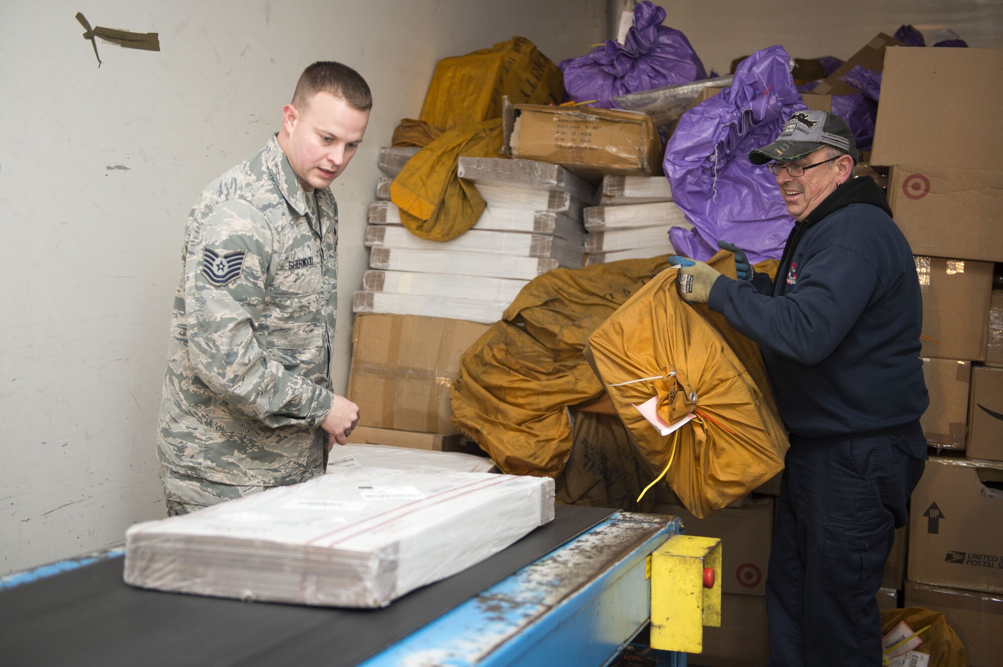 U.S. Air Force Tech. Sgt. Jedediah Sherwood, Detachment Five, Assistant Detachment Chief, loads packages on a conveyer belt, at RAF Alconbury, Dec. 19, 2017. The packages are then separated according to APO. (U.S. Air Force photo by Airman 1st Class Chase Sousa)