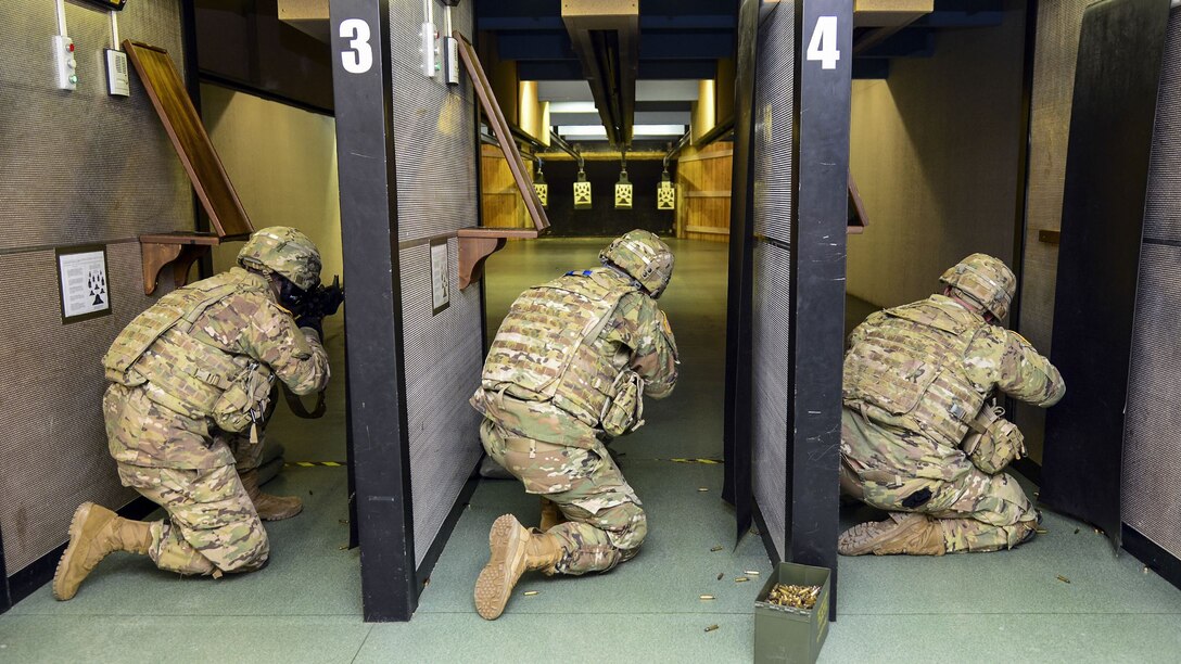Three soldiers kneel while firing at targets.