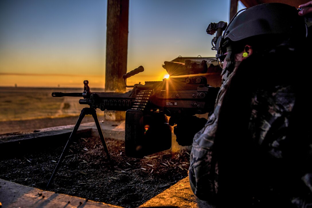 An airman fires a weapon with the sun behind the weapon.