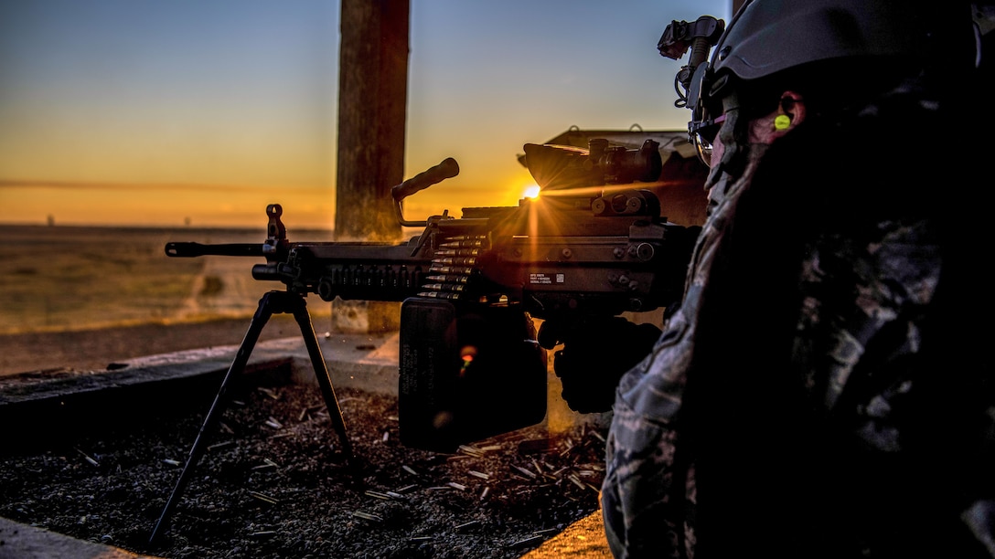 An airman fires a weapon with the sun behind the weapon.