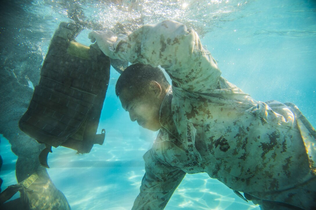 A Marine swims underwater holding gear.