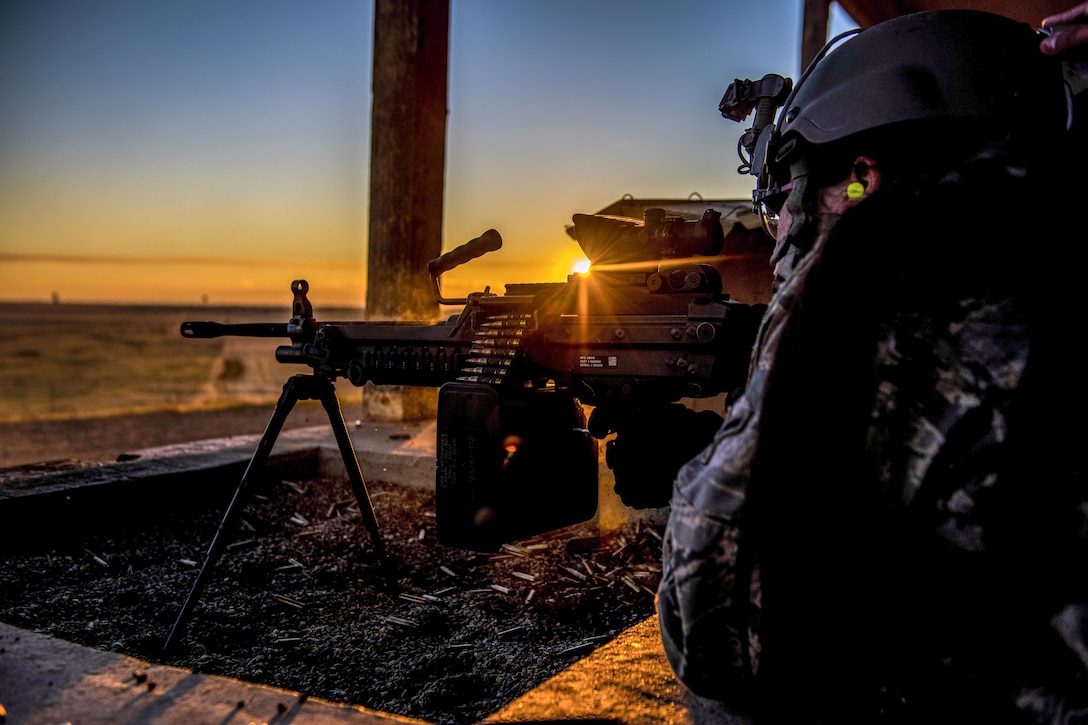 An airman fires a weapon with the sun behind the weapon.