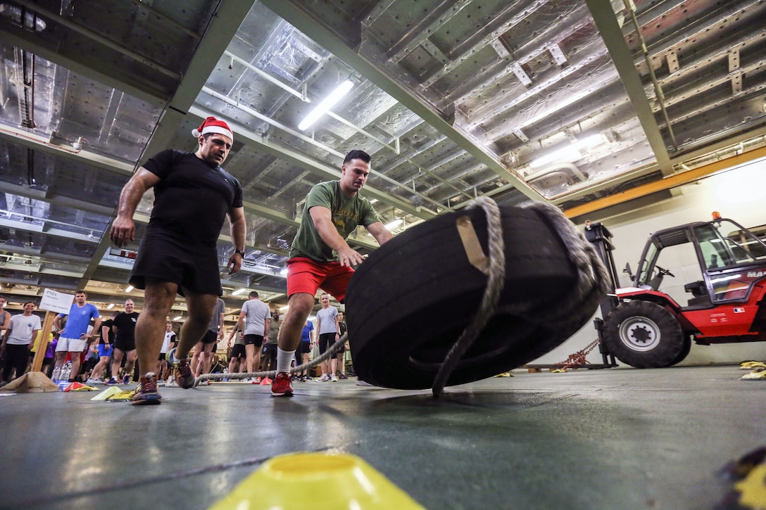 A Marine appears to push over a tire in a ship's interior as another service member watches.