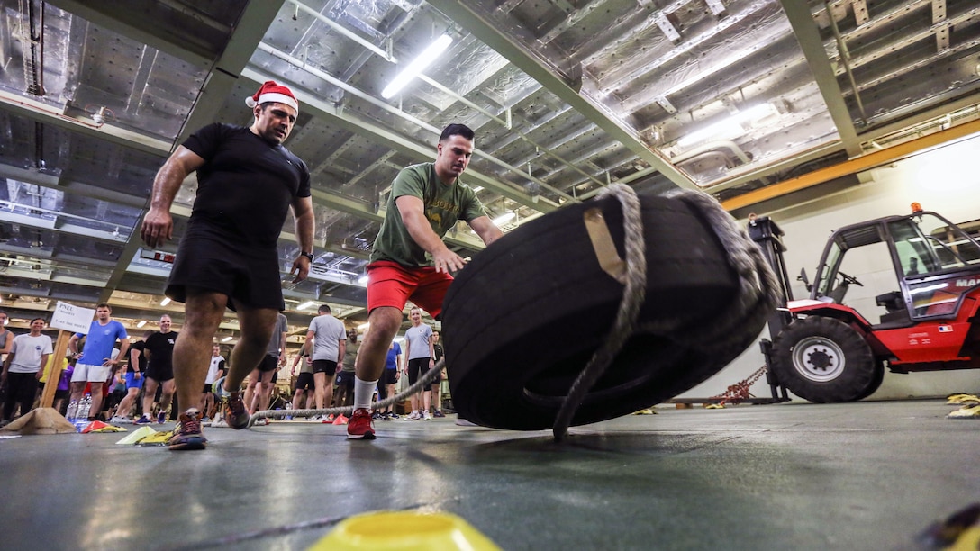 A Marine appears to push over a tire in a ship's interior as another service member watches.